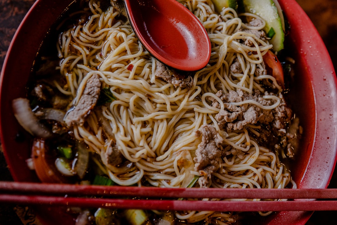 A steaming bowl of Bún Bò Huế with rich amber broth, thick noodles, and fresh herbs